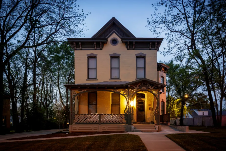 The Elkins House at dusk with the porch lantern lit and trees on either side