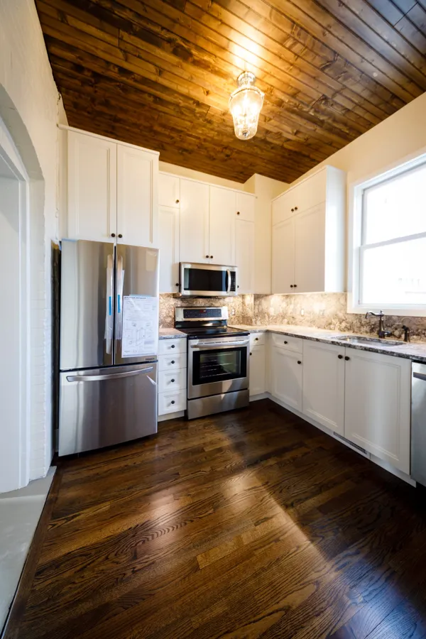 A white kitchen under a stained wood plank ceiling