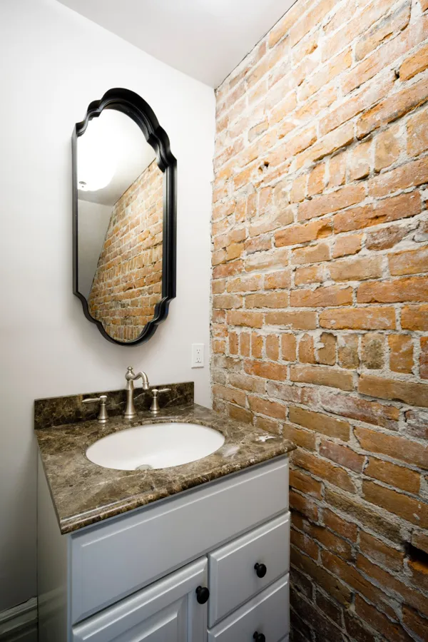 A powder room with an exposed brick wall and a black arched mirror