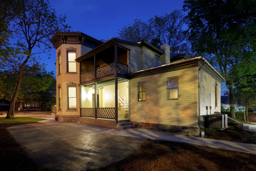 The two-story rear porch and frame addition lit at dusk